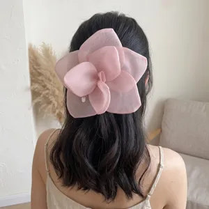 Detailed back view of an oversized pink mesh rose flower hair clip on wavy dark hair.