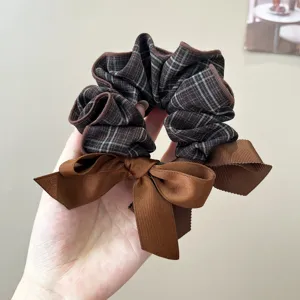 Close-up of a brown plaid fabric scrunchie with a matching ribbon bow detail.