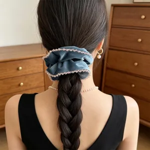Nahaufnahme eines blauen Samt-Scrunchies mit Kristallperlen in einer Flechtfrisur.