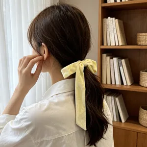 Elegant yellow velvet bow hair tie with long ribbon shown on model's ponytail back view