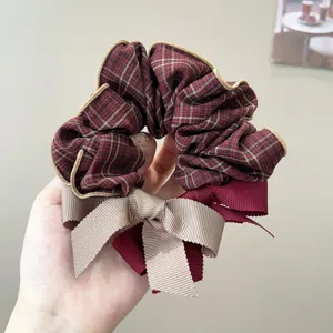 Close-up of a plaid scrunchie with a dual-color ribbon bow and elegant gold piping.