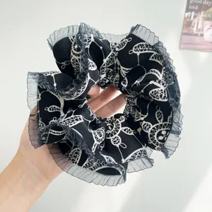 Close-up of black oversized scrunchie with lace edge and white patterns