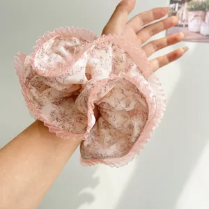 Close-up detail of a large pink floral scrunchie with pleated lace edges on a wrist.