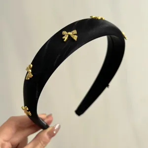 Detailed view of a thick black satin headband featuring small decorative golden metal bows.