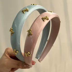 Detailed view of two satin padded headbands with gold bow accents in pink and blue.