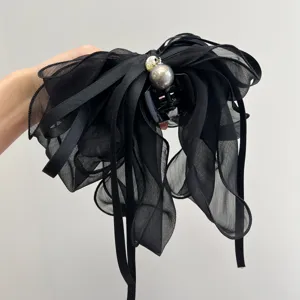 Detalle de una pinza para el cabello con lazo de malla negra y una elegante perla gris.