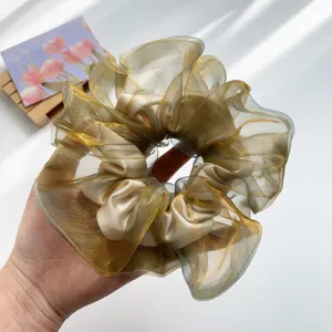 Detailansicht eines schimmernden Organza-Haargummis in Gold und Blau.