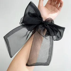 Nahaufnahme eines großen schwarzen Organza-Haargummis am Handgelenk mit transparenter Textur.