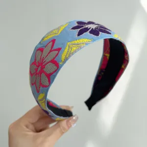 Detailed view of bohemian style light blue fabric headband with colorful floral embroidery