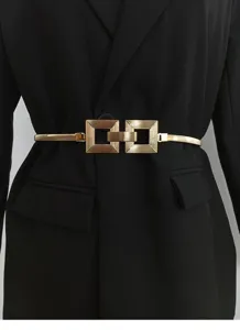 Vista en detalle de cinturón elástico de mujer con hebilla cuadrada de metal dorado en blazer negro.