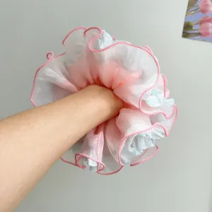Detailaufnahme eines großen rosa-blauen Haargummis aus Netzstoff am Handgelenk.