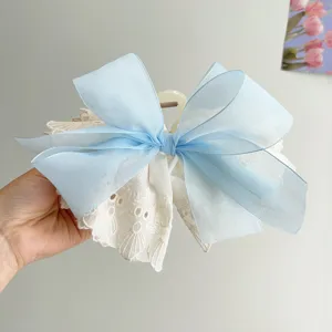Close-up detail of a large double-layered bow hair claw clip with blue organza and white lace.