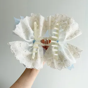 Close-up detail of a large white embroidered lace bow hair claw clip with blue ribbon
