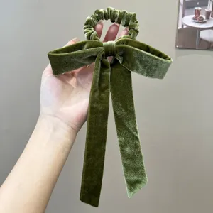 Macro view of a luxurious green velvet bow scrunchie held in hand, showing detail