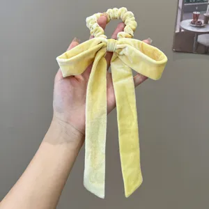 Detail view of a yellow velvet bow scrunchie with elegant long ribbons for hair