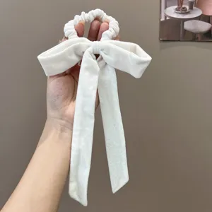 Close-up view of a luxury off-white velvet bow scrunchie with long streamers held by hand