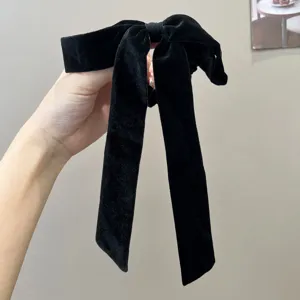 Elegant black velvet bow hair tie with long streamers shown in a handheld close-up view