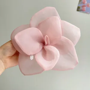 Detail of a large pink organza flower hair accessory held in hand showing sheer texture
