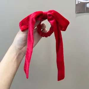 Close-up of elegant red velvet bow scrunchie with long ribbons for hair styling.