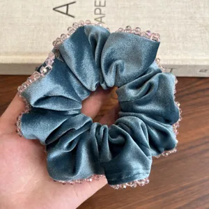 Detailansicht eines luxuriösen blauen Samt-Haargummis mit funkelnden rosa Kristallperlen.