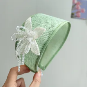 Detailed macro view of the intricate white bead-work flower on a green wide headband.