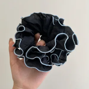 Detalle de un coletero de organza negro con bordes de volantes en color azul claro.