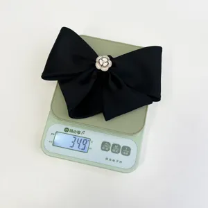 Macro view of black satin bow hair clip with camellia weighing 34.9g on a scale