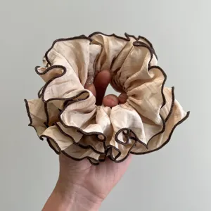Primer plano de un coletero beige con volantes y elegantes bordes ribeteados café oscuro.