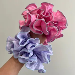 Vista detallada de dos coleteros de organza plisada en rosa y lila puestos en la muñeca