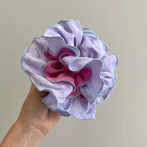 Primer plano de un coletero de volantes en lavanda y rosa sostenido por una mano humana