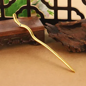 Detailed view of a golden wavy hair stick with rhinestone on a wooden stand