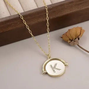 Gros plan d'un collier pendentif rond tournant doré avec la lettre K sertie de strass brillants.