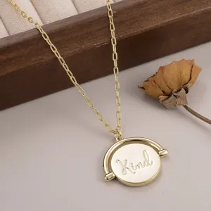 Vue macro montrant le collier pendentif circulaire doré rotatif avec gravure 'Kind' détail