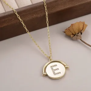 Gros plan d'un collier en or avec un pendentif rond rotatif et la lettre E en strass