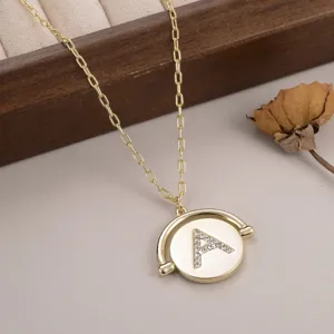 Détail d'un collier doré minimaliste avec un pendentif circulaire et la lettre A en strass
