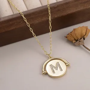 Détail d'un collier doré avec pendentif circulaire rotatif orné d'une lettre M en strass.