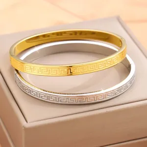 Dettaglio di bracciali rigidi in acciaio inossidabile oro e argento con motivo greco