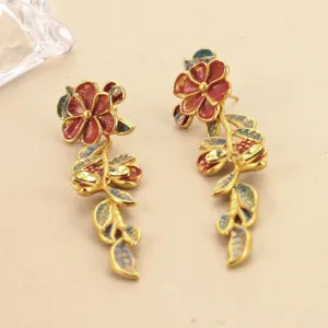 Makroansicht der komplizierten roten Emaille-Blumen und goldenen Blattdetails auf Retro-Ohrringen.