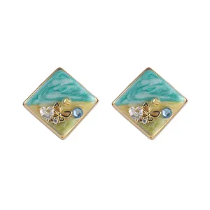 Gros plan de boucles d'oreilles carrées en émail avec détails papillon et cristal.
