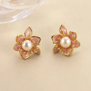 Close-up of pink enamel flower earrings with central white pearls and gold accents