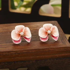 Détail macro de boucles d'oreilles fleurs en émail faites main avec perle centrale