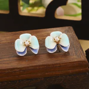 Gros plan détaillé sur des boucles d'oreilles fleurs émaillées avec perle naturelle.