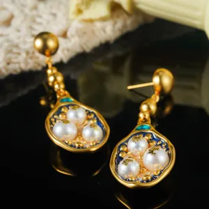 Detail van gouden vintage oorbellen met witte parels en blauw emaille inlegwerk.