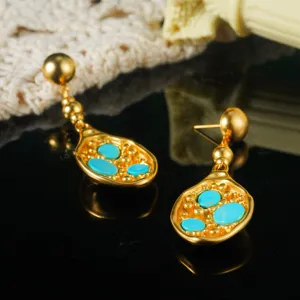 Detailopname van vintage goudkleurige oorbellen met turquoise inleg op donkere plaat