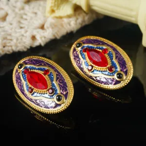 Gedetailleerde close-up van vintage gouden oorbellen met rood kristal en emaille
