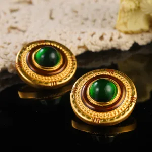 Detailed view of vintage palace style gold earrings with emerald green central gems.