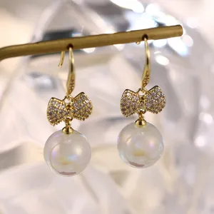 Elegante goldfarbene Schleifenohrringe mit irisierenden Perlen und Zirkonia-Steinen.