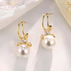 Elegante goldene Schleifenohrringe mit weißen Perlen und funkelnden Kristalldetails.