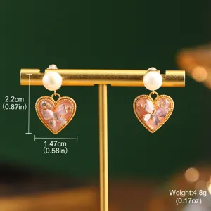 Close-up of heart-shaped earrings featuring natural pearls and pink enamel butterfly motif.