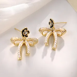 Detailansicht eleganter goldener Schleifenohrringe mit schwarzen Kamelien und Perlen